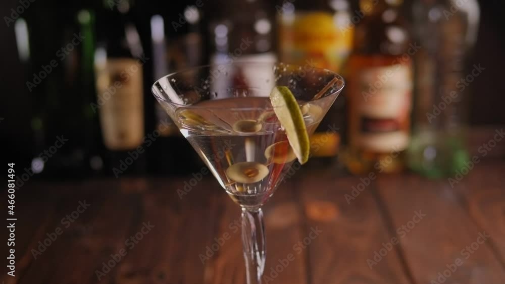 Close-up of green olives and lime in a Martini glass in a bar on a blurred background of bottles, the glass slowly rotates in a circle. Slow motion. Close-up of green olives and lime in a Martini glass in a bar on a blurred background of bottles, the glass slowly rotates in a circle. Slow motion.