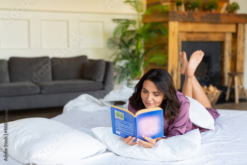 Digital detox concept - a middle-aged woman is resting while lying in bed while reading a book.