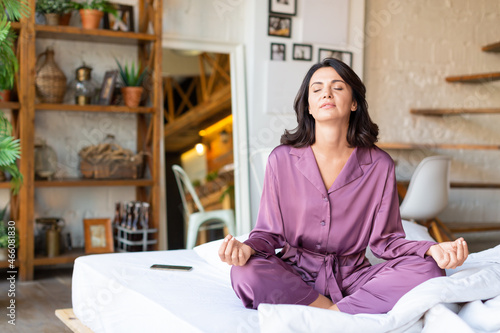 Mental health and digital detox concept - middle aged woman meditating in bed.