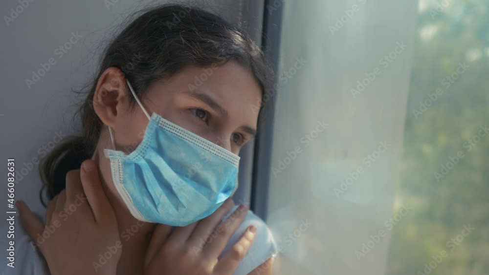 Portrait of girl sick corona virus. little teenager girl in a medical mask is sad at the window hugs herself over the shoulders Coronavirus, quarantine isolation concept. lifestyle Coronavirus Portrait of girl sick corona virus. little teenager girl in a medical mask is sad at the window hugs herself over the shoulders Coronavirus, quarantine isolation concept. lifestyle Coronavirus