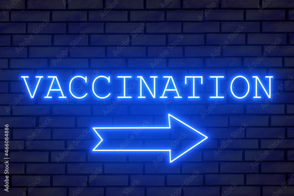 Obraz premium Neon sign VACCINATION on a brick wall. A neon arrow indicates a vaccination station.