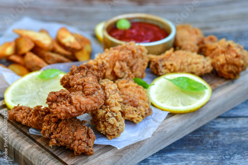 
 Crispy  deep fried   chicken strips and Wings ,onions and Wedges potatoes  Breaded  with cornflakes chicken  breast fillets  with chilly peppers and fresh   basil on wooden rustic background