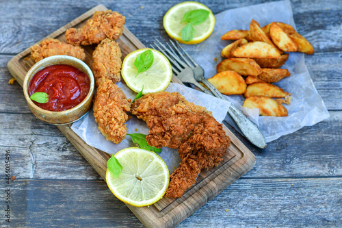  Crispy deep fried chicken strips and Wings ,onions and Wedges potatoes Breaded with cornflakes chicken breast fillets with chilly peppers and fresh basil on wooden rustic background