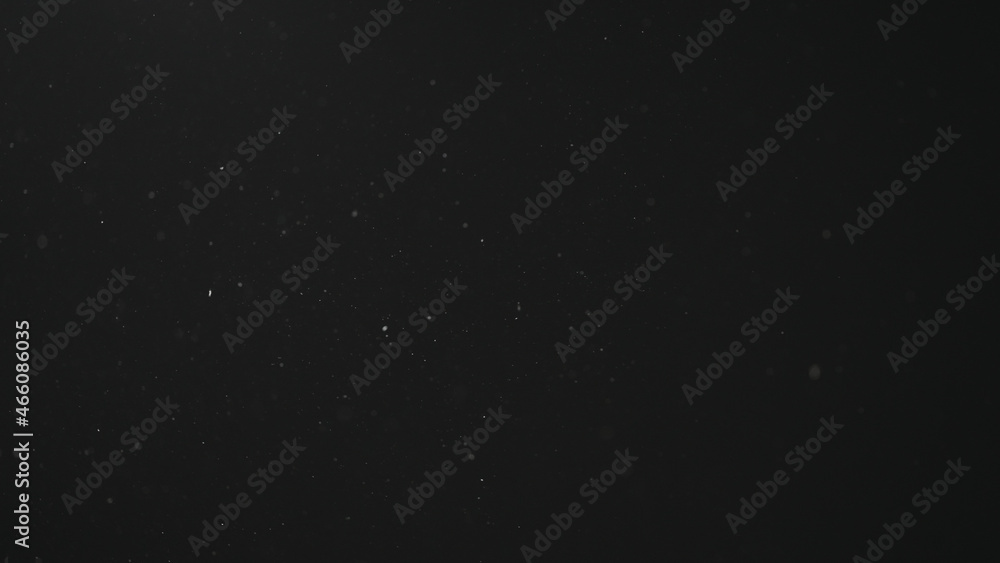 Dust particles float in neutral light on black background Dust particles float in neutral light on black background