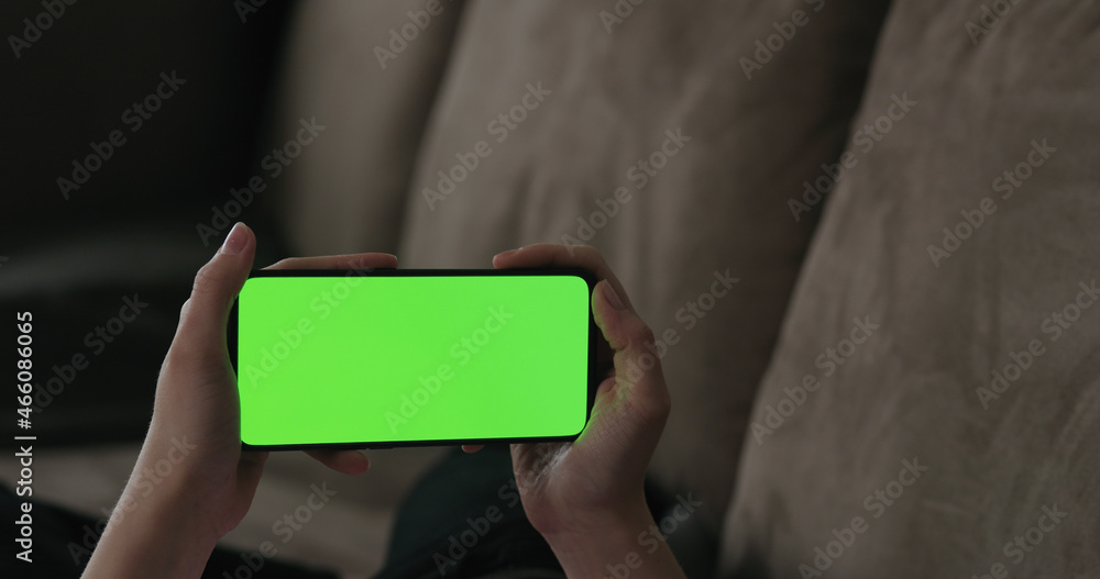 Young woman lying on a couch and using smartphone with horizontal green screen Young woman lying on a couch and using smartphone with horizontal green screen
