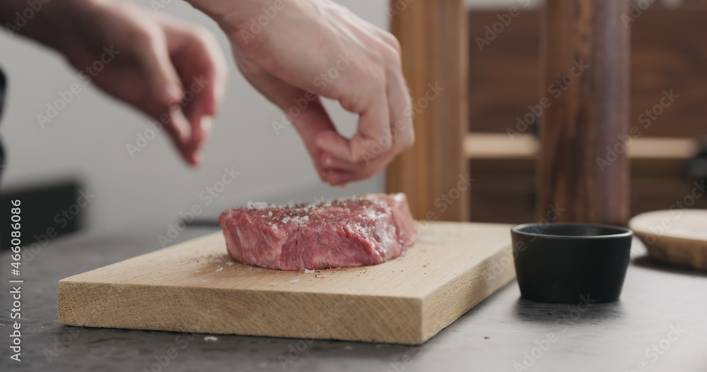 Man seasoning raw ribeye steak on oak wood board Man seasoning raw ribeye steak on oak wood board