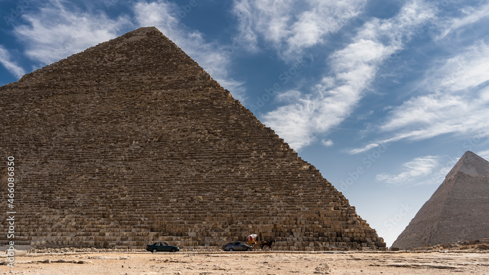 Two great pyramids of Giza on the background of a blue sky with picturesque clouds. At the foot there are modern cars, a horse harnessed to a cart. Cairo. Egypt