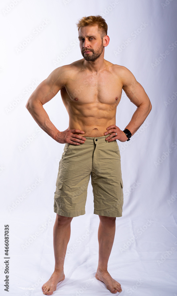 Fototapeta premium muscular man in shorts posing, shows, straining muscles. gray background