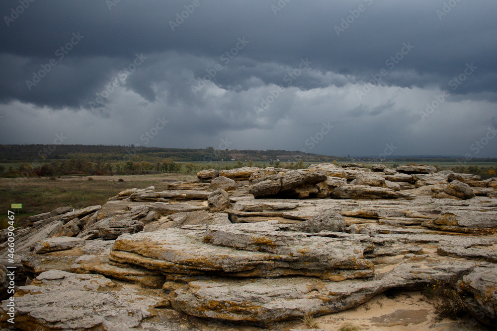 Huge ancient stones of the Stone Tomb megalith on the ground against the background of storm clouds and fields