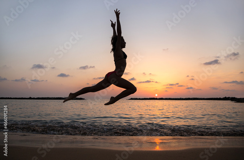 Happy young slender woman jumping and having fun at sunset on the beach by the sea. Freedom and happiness concept. The girl trains with pleasure. Energy, strength, youth, healthy lifestyle