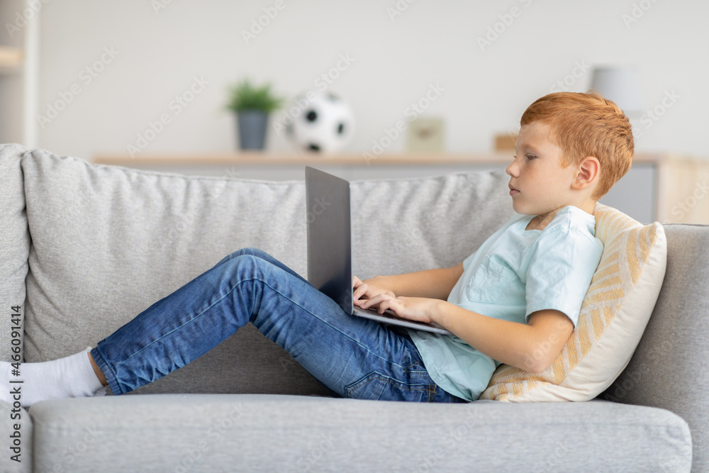 Redhead boy using laptop, playing online video game, side view Redhead boy using laptop, playing online video game, side view