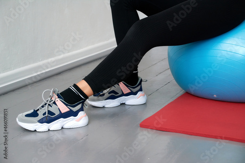close-up of a woman sitting on a blue sports ball, with his feet on a red yoga mat.
