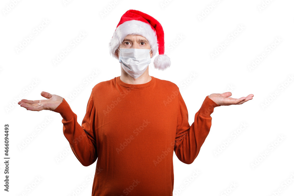 an isolated shot of a surprised man in a medical mask, in casual clothes, a Christmas hat cap. He spread his arms to the sides and raised his shoulders, I don't know, he looks into the camera an isolated shot of a surprised man in a medical mask, in casual clothes, a Christmas hat cap. He spread his arms to the sides and raised his shoulders, I don't know, he looks into the camera