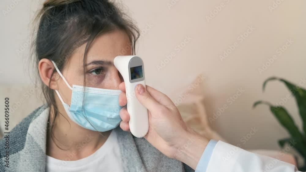 The doctor measures the temperature of a non-contact infrared thermometer. Male nurse checking temperature to young woman during home visit. Close-up The doctor measures the temperature of a non-contact infrared thermometer. Male nurse checking temperature to young woman during home visit. Close-up
