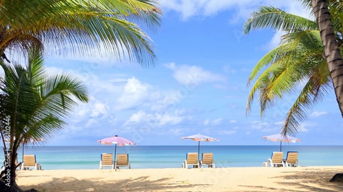 Beach with palm trees and umbrellas to sit and relax on a sunny day at Karon Beach, Phuket, Thailand.