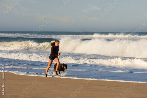 beautiful young athletic woman running with her dog on the beach photo