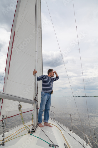 Man is sailing  yacht and looking through binoculars