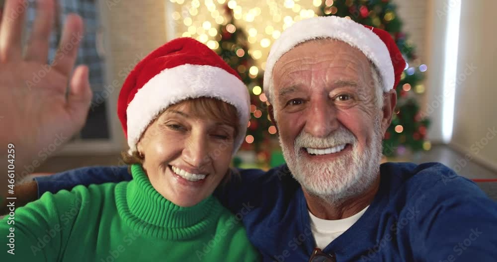 Happy senior male with gray beard hugging mature woman while she is waving at camera greeting for New Year celebration at home Happy senior male with gray beard hugging mature woman while she is waving at camera greeting for New Year celebration at home