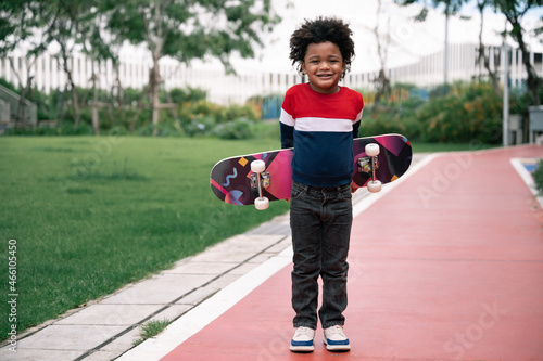 Happy kid boy with afro hair and skateboard in the park