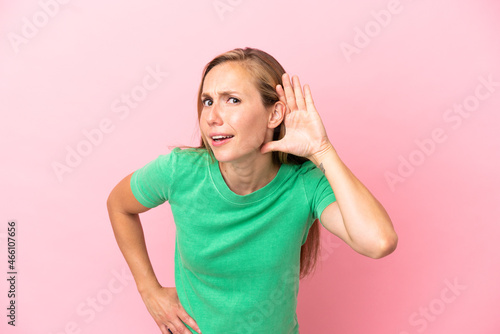 Young English woman isolated on pink background listening to something by putting hand on the ear