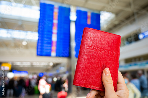 Woman holding a passport against the background of an airport information board.