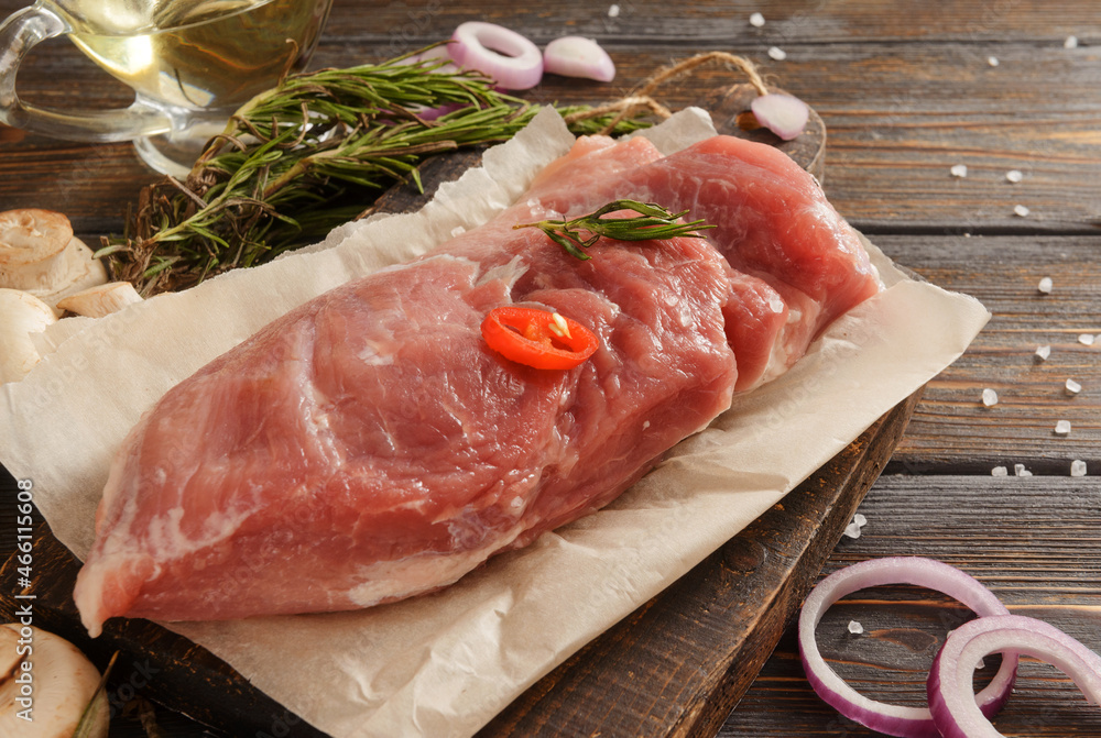 raw pork tenderloin with  chili pepper, onion, olive oil, rosemary on a dark wooden