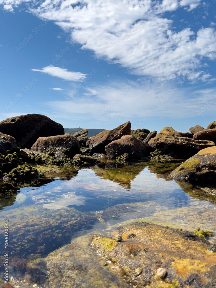 A small water pond with clear reflection surrounded by sea rocks at the coast next to the sea, Palm Beach NSW Australia 