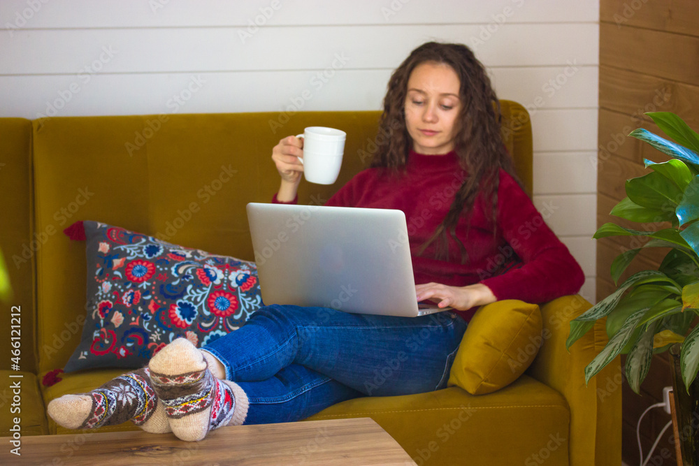 Pretty white young woman relaxing on couch in cozy green space home atmosphere. A girl with cup of tea, coffee in hand and laptop. Online socializing, shopping, remote work. People in the interior. Pretty white young woman relaxing on couch in cozy green space home atmosphere. A girl with cup of tea, coffee in hand and laptop. Online socializing, shopping, remote work. People in the interior.