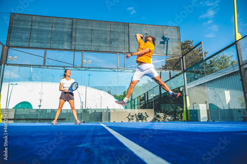 Mixed padel match in a blue grass padel court - Beautiful girl and handsome man playing padel outdoor