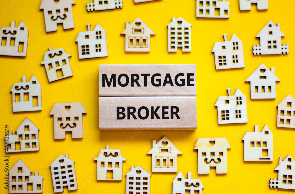 Mortgage broker symbol. Concept words 'Mortgage broker' on wooden blocks near miniature wooden houses. Beautiful yellow background. Business, mortgage broker concept.