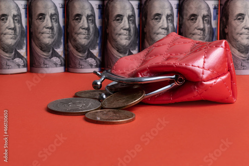 American coins pouring out of a miniature red wallet against a background of rolled up American 100 dollar bills standing against a red background photo