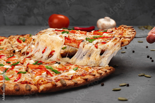 A woman's hand takes a slice of pizza with a spatula and the cheese stretches savorily, close-up.