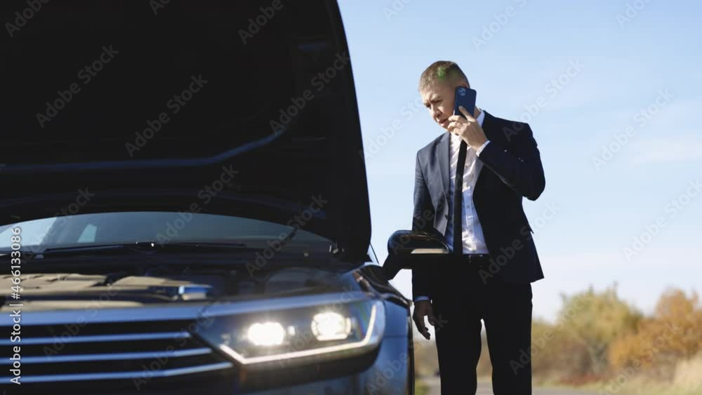 Dissapointed businessman talking on phone. Broken car with opened hood stand besides. Helpless man need help and assistance. Electric car accident. Car trouble. Young man outside car. Dissapointed businessman talking on phone. Broken car with opened hood stand besides. Helpless man need help and assistance. Electric car accident. Car trouble. Young man outside car.