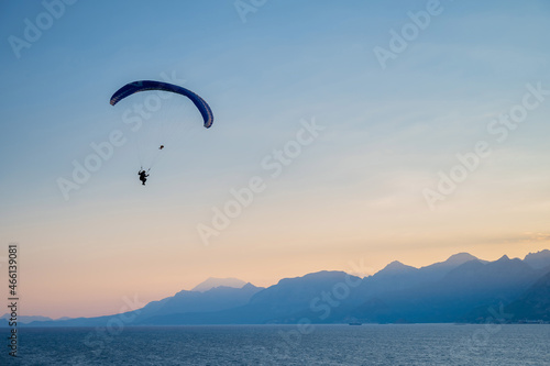 Silhouette of a man on a paraglider flying over the sea at sunset.