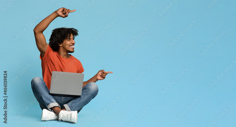 Happy black man with laptop pointing at copy space