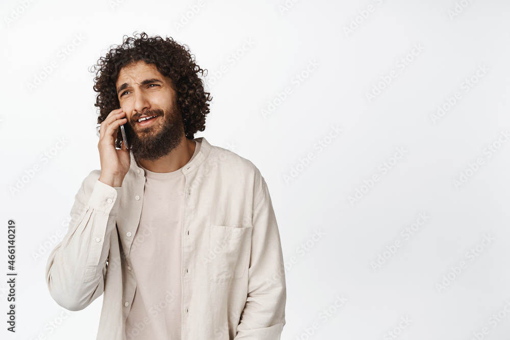 Smiling handsome middle eastern guy talking on mobile phone, having a call, standing over white background Smiling handsome middle eastern guy talking on mobile phone, having a call, standing over white background