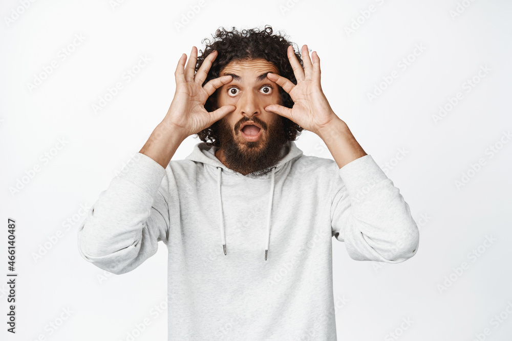Shocked hispanic man widen his eyes in awe, cant believe, looking with disbelief and amazement at camera, standing startled over white background Shocked hispanic man widen his eyes in awe, cant believe, looking with disbelief and amazement at camera, standing startled over white background
