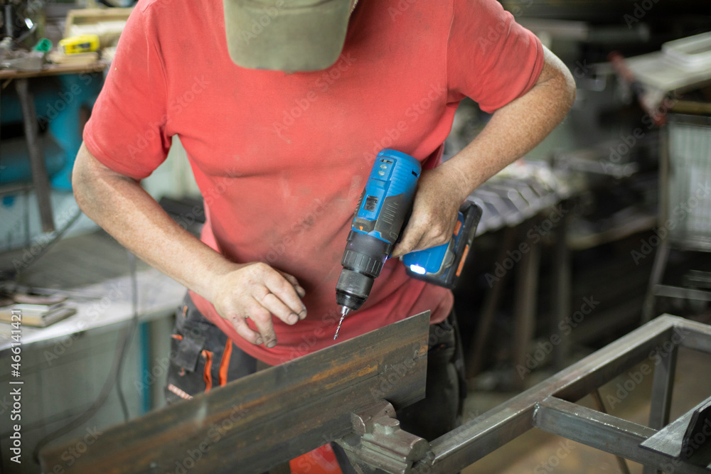 A worker in a gray cap and a red T-shirt works with a screwdriver. Close-up, front view. Metal construction.