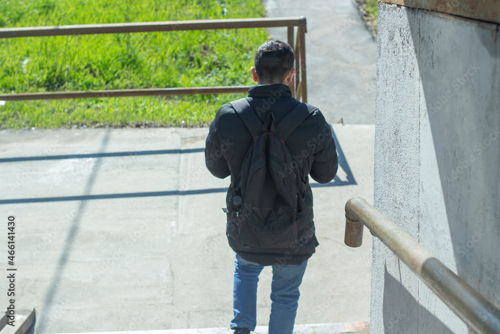 A man in casual clothes with a backpack goes down the stairs. Sunny day, early autumn.