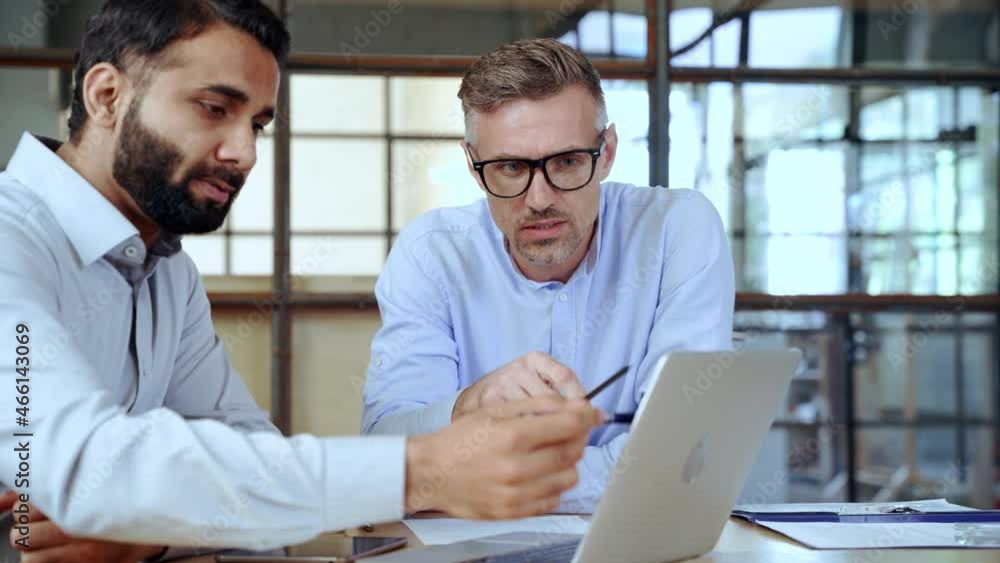 Two diverse business men discussing financial market data using laptop and digital tablet. Financial advisor broker manager consulting investor client about digital investment at office meeting. Two diverse business men discussing financial market data using laptop and digital tablet. Financial advisor broker manager consulting investor client about digital investment at office meeting.