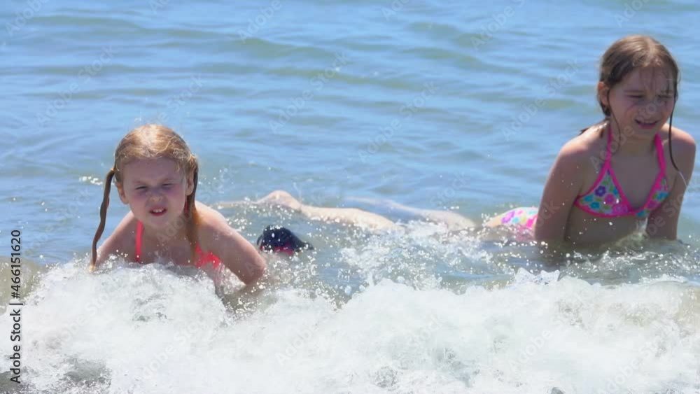 Two little happy girls are laying in splashing sea waves on the beach Two little happy girls are laying in splashing sea waves on the beach