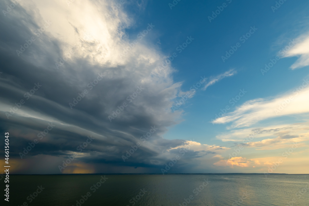 Overcast sky and heavy storm clouds over a wide river at sunset. Rain passing in the distance.