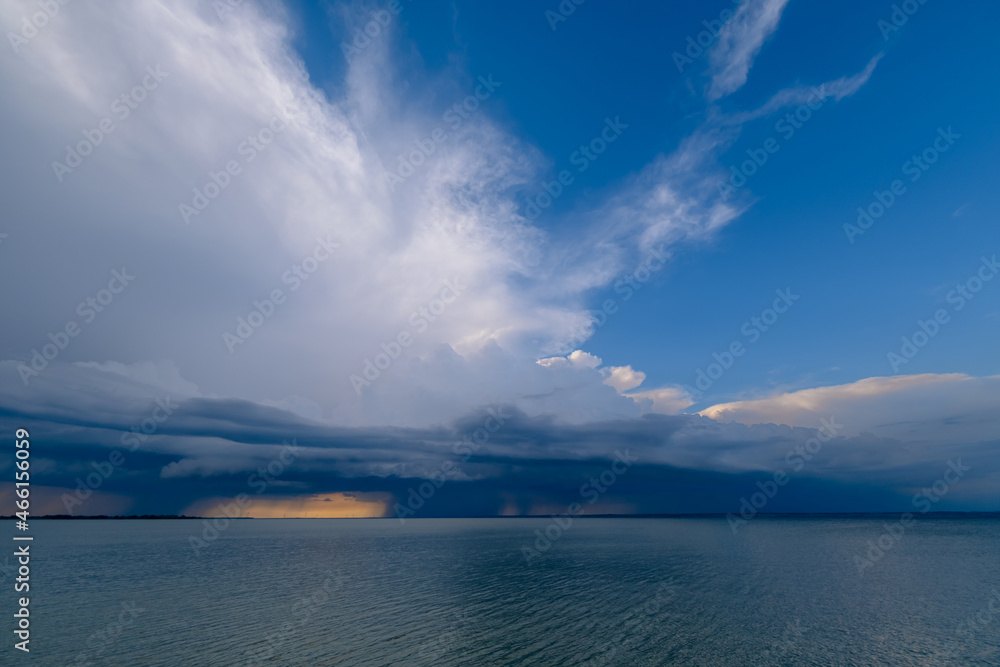 Overcast sky and heavy storm clouds over a wide river at sunset. Rain passing in the distance.