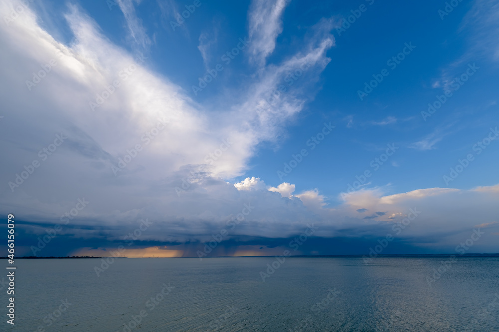 Overcast sky and heavy storm clouds over a wide river at sunset. Rain passing in the distance. Overcast sky and heavy storm clouds over a wide river at sunset. Rain passing in the distance.