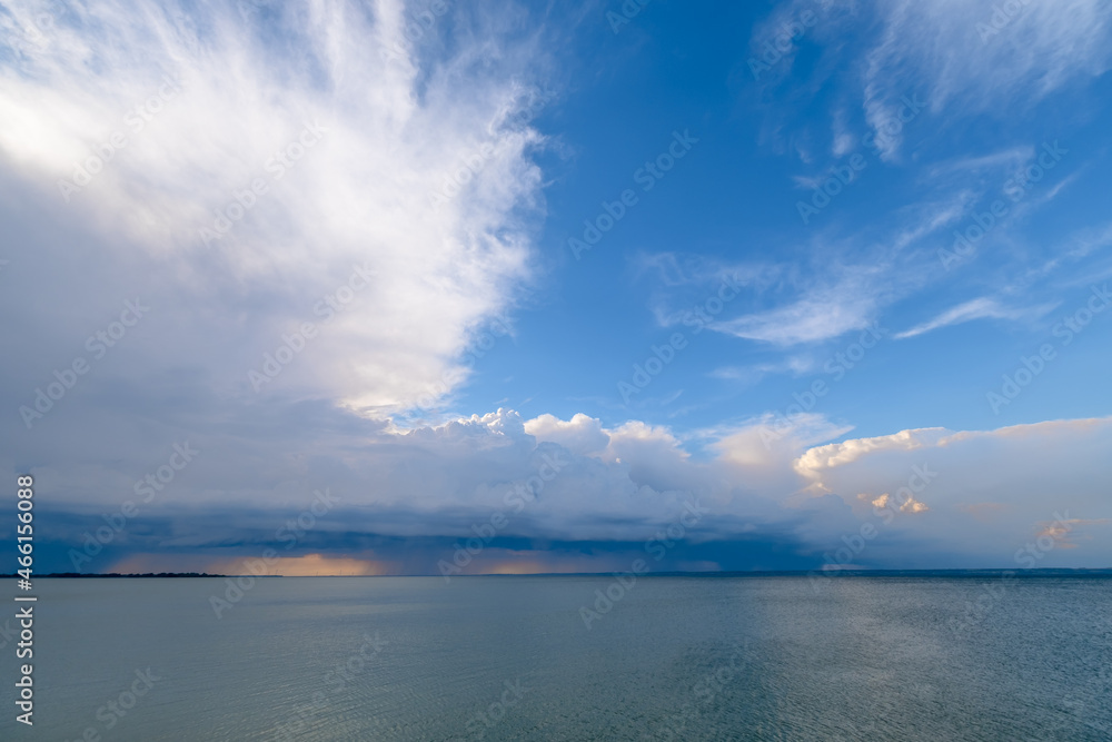 Overcast sky and heavy storm clouds over a wide river at sunset. Rain passing in the distance. Overcast sky and heavy storm clouds over a wide river at sunset. Rain passing in the distance.