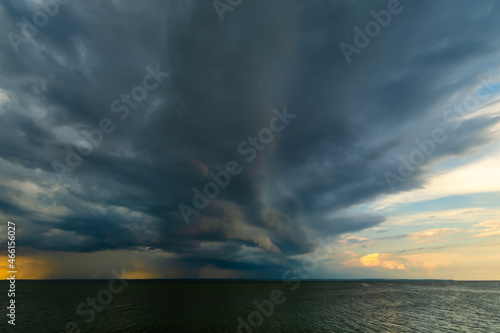 Overcast sky and heavy storm clouds over a wide river at sunset. Rain passing in the distance. © Danil Evskiy
