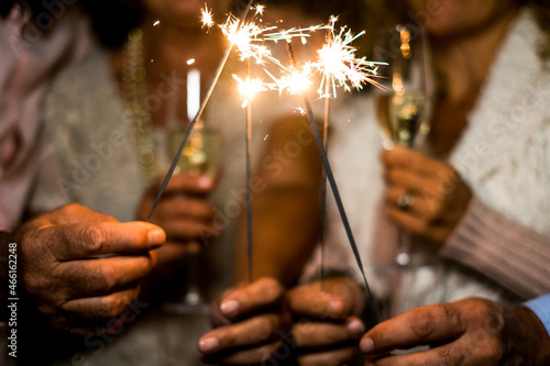group of four people enjoying new year night celebrating with sparklers in the middle and looking at the camera - adults having fun together