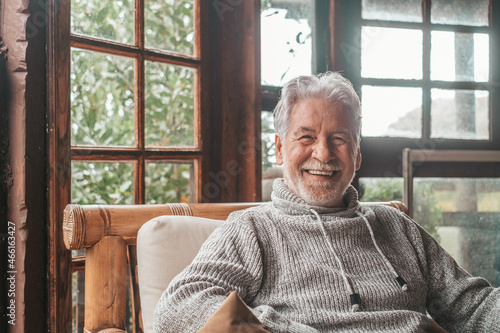 Portrait of old man smiling and looking at the camera sitting on the sofa from home. Closeup male person senior cheerful indoor.. photo