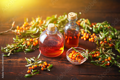 Glass bottle with sea buckthorn oil berries and sea buckthorn branches on wooden background photo