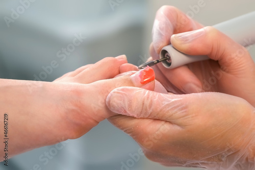Pedicurist woman removes shellac polish from toes using manicure machine, closeup view. Pedicure Master is removing red gel polish from nails on toes using electric nail drill in cosmetology.